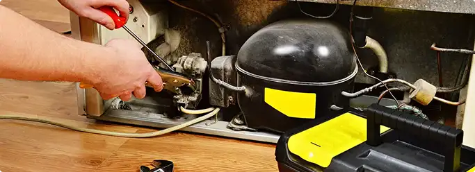 Refrigerator repair technician fixing the compressor and wiring in Liverpool, NY