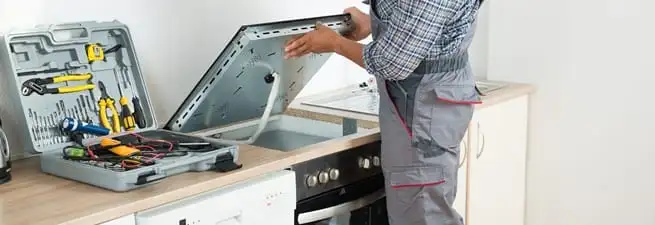 Cooktop repair technician lifting a built-in stovetop for service in Syracuse, NY