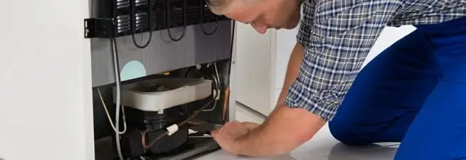 Refrigerator repair technician servicing the compressor and condenser area in Syracuse, NY