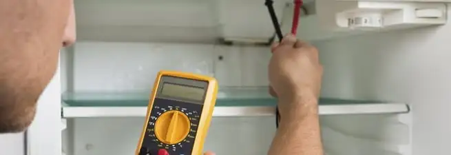 Refrigerator repair technician testing electrical components with a multimeter in Syracuse, NY